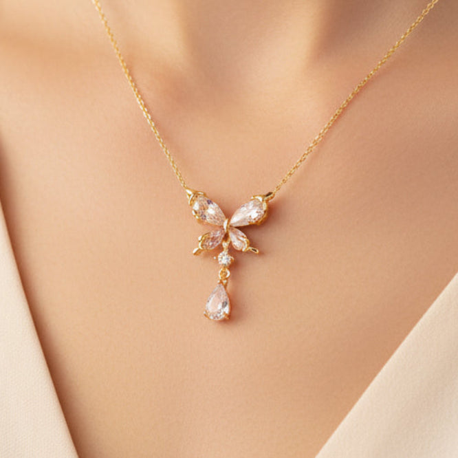 Gold necklace with a bow and teardrop pendant on a white background