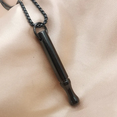 Black metal whistle pendant on a chain against a beige fabric background