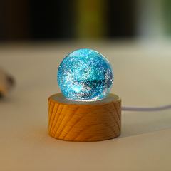 A glowing blue glass orb with swirling nebula patterns, displayed on a wooden lighted base.