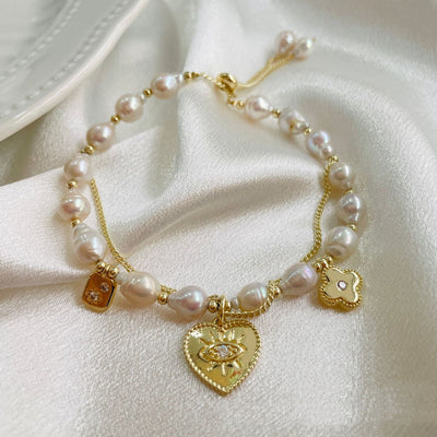 Pearl bracelet with gold heart-shaped charms on a white fabric background