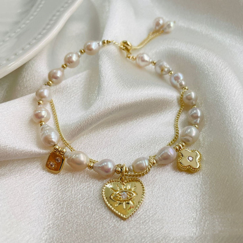Pearl bracelet with gold heart-shaped charms on a white fabric background