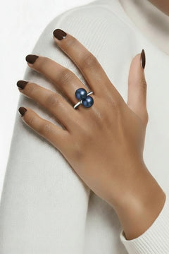 Hand wearing a sterling silver ring with two midnight blue pearls against a cream fabric sweater background.