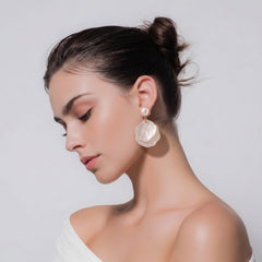 Woman wearing white mother‑of‑pearl double shell dangle earrings with gold‑tone metal accents plain background.