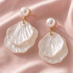 Mother‑of‑pearl double shell dangle earrings with white shell drops and gold‑tone metal accents on a pale pink background.