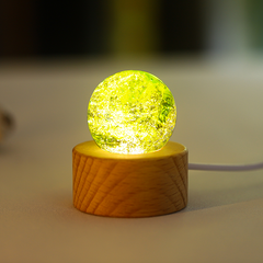 A green glowing glass sphere with galaxy‑like internal patterns, placed on a wooden base.