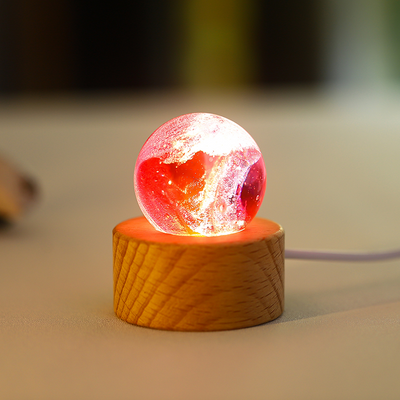 A red illuminated glass sphere resembling a solar flare pattern, resting on a wooden LED base.