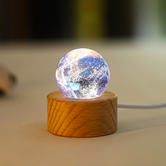 A white and blue translucent glass orb with frosted lunar‑style textures, illuminated on a wooden base.