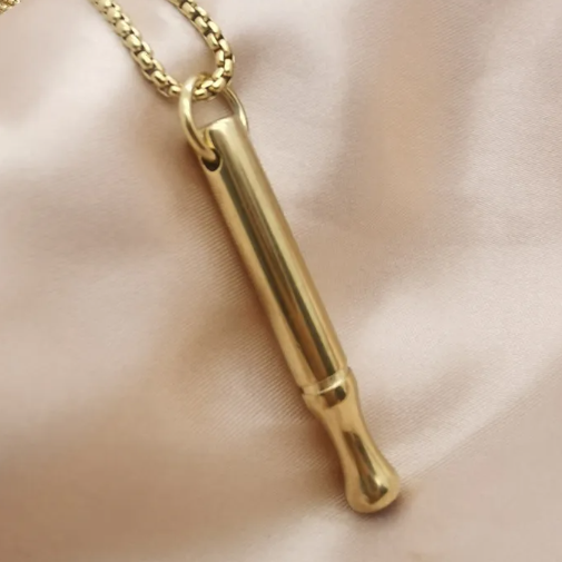 Gold cylindrical pendant on a chain against a beige background