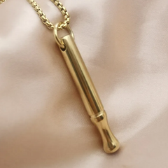 Gold cylindrical pendant on a chain against a beige background