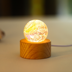 A warm yellow glass orb with starburst textures, lit from below on a wooden stand.