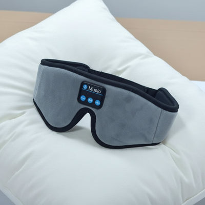 Gray sleep mask with Bluetooth controls on a white pillow