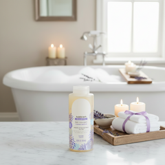 Lavender bubble bath bottle on a marble counter beside towels, candles, and fresh lavender, with a bubble‑filled tub in the background creating a calm, spa‑like atmosphere.