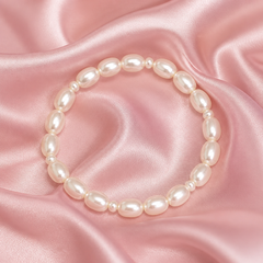 White oval‑pearl bracelet displayed in a circular shape on soft pink satin fabric with gentle folds, highlighting the pearls’ smooth luster and elegant simplicity.