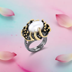 An artistic claw‑set silver ring featuring an 8×10mm natural baroque freshwater pearl, shown against a soft pastel pink‑blue‑purple background with scattered rose petals.
