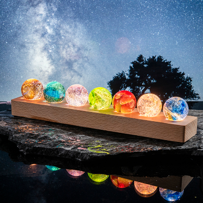 A full set of glowing glass spheres in various colors arranged on a wooden holder.