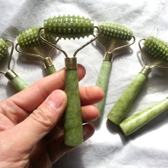 Green skin care roller tools on a white background with a hand holding one tool.