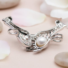 An open silver pendant put featuring a white pearl inside, displayed on a light peach background
