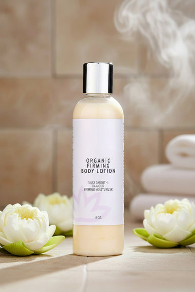 Organic firming body lotion bottle displayed on a spa-inspired tiled surface with steam, white lotus flowers, and folded towels creating a clean, calming self-care scene.