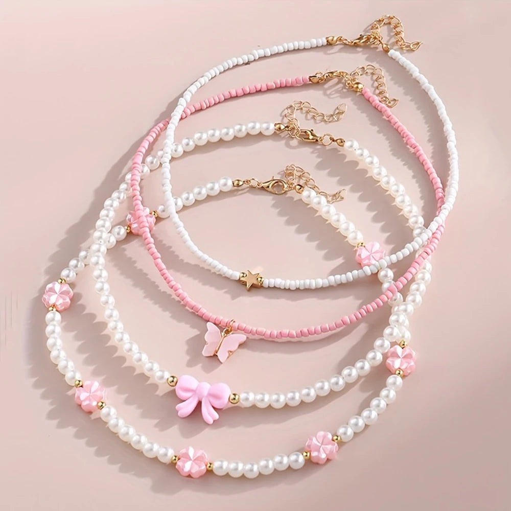Delicate pastel necklaces with pearls, beads, and butterfly, bow, star, and flower charms arranged on a soft pink background.
