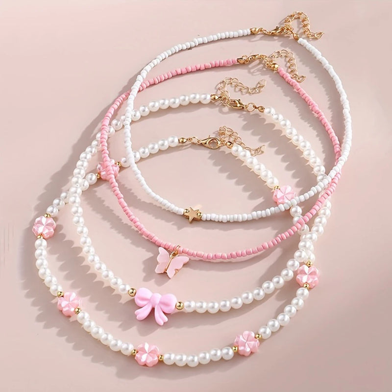 Delicate pastel necklaces with pearls, beads, and butterfly, bow, star, and flower charms arranged on a soft pink background.
