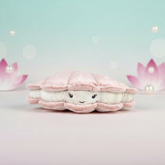 Pink seashell plush with a smiling pearl face, displayed on a soft aqua‑pink boutique background with floating pearls and lotus accents.