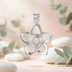 A close-up of the back of a silver-toned metal flower-shaped charm or pendant on a white background with green leaves and white flower petals scattered about