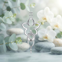 A close-up of the back of a silver-toned metal flower-shaped charm or pendant on a white background with green leaves and white flower petals scattered about