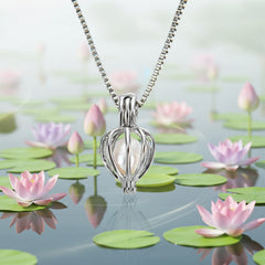 Silver cage pendant holding a white pearl suspended above calm water with lotus flowers and lily pads, creating a serene and elegant jewelry presentation.