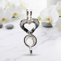 A close-up open view of a silver-toned metal heart-shaped charm or pendant on a white background with green leaves and white flower petals scattered about