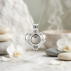 A close-up of the back of a silver-toned metal heart-shaped charm or pendant on a white background with green leaves and white flower petals scattered about