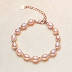 A pink chain bracelet with irregular light pink freshwater pearls and small rose gold spacer beads, displayed on a textured beige background.