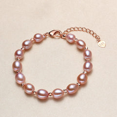 A purple pearl bracelet featuring freshwater pearls and small rose gold spacer beads, complete with a lobster clasp, extender chain, and a heart-shaped tag engraved with '925'.