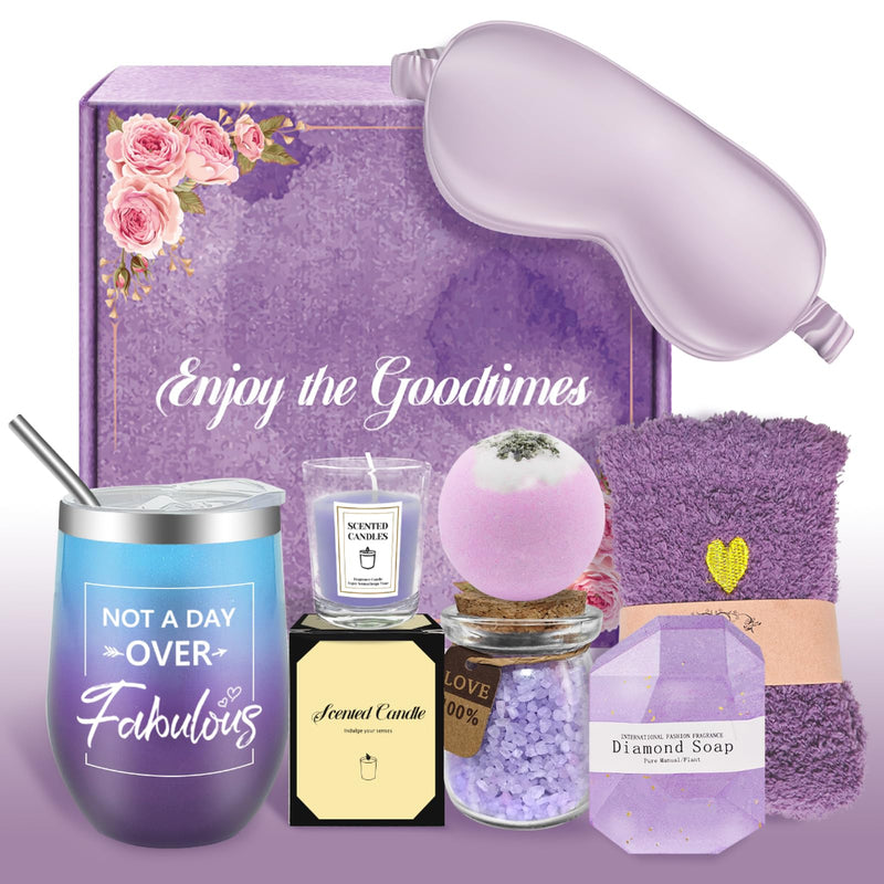 Purple-themed spa gift set with a satin sleep mask, gradient tumbler, scented candle, bath bomb, bath salts, fuzzy socks, and diamond-shaped soap arranged in front of a floral gift box.