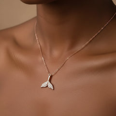A rose gold mermaid tail pendant necklace adorned with small clear crystals, resting on a dark skinned neckline.
