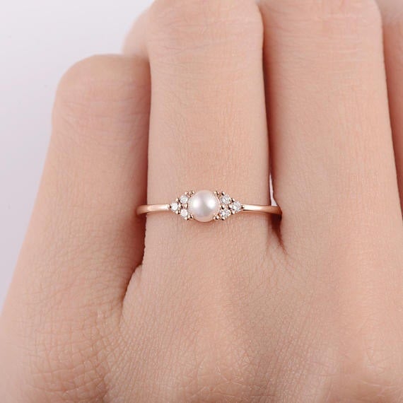 Rose gold ring with a pearl on a hand against a light background