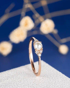 Rose gold ring with a pearl and small diamonds on a white stand with a blue background