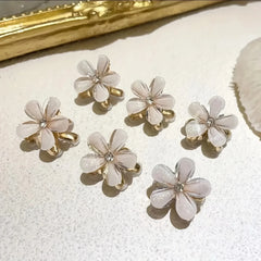 Set of six flower-shaped rings with gold accents on a textured white surface.