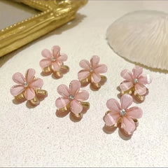 Set of pink flower-shaped earrings on a textured surface with a gold frame and shell in the background.