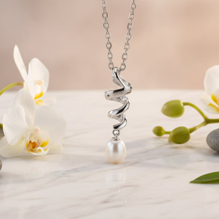 A silver-toned necklace with a twisted heart pendant and a single white pearl drop, displayed on a dark textured surface.