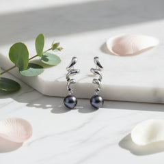 A pair of silver-toned spiral drop earrings with dark baroque pearls hanging from the ends, displayed on a black textured surface.