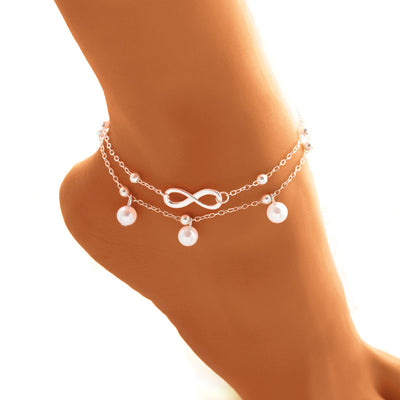 Anklet jewelry with pearls and an infinity symbol on a foot against a white background