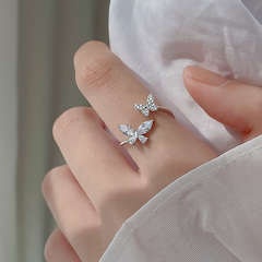 Silver butterfly ring on a person's finger with a neutral background