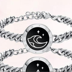 Silver chain bracelet with black circular design featuring a moon and star symbol on a light pink background.