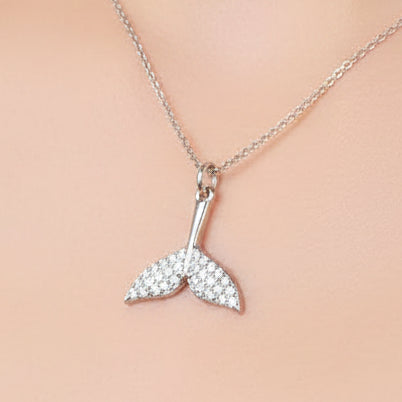 A silver mermaid tail pendant necklace covered in small clear crystals, resting on a cream-colored skin neckline.