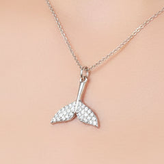 A silver mermaid tail pendant necklace covered in small clear crystals, resting on a cream-colored skin neckline.