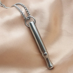 Silver cylindrical pendant on a chain against a beige fabric background