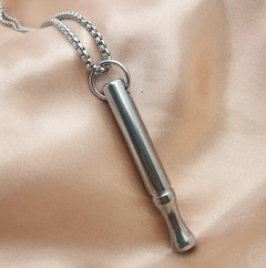 Silver cylindrical pendant on a chain against a beige fabric background