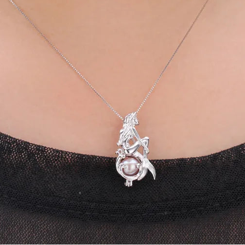 A silver pendant necklace featuring a mermaid design with a pearl, shown worn on a model's neck over a black top.