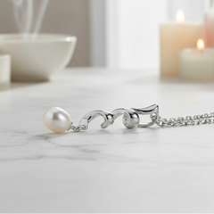 A silver pendant necklace featuring a single white pearl suspended from a polished silver clasp and chain, set against a dark black background.
