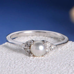 Silver ring with a pearl and small diamonds on a textured surface with blue background